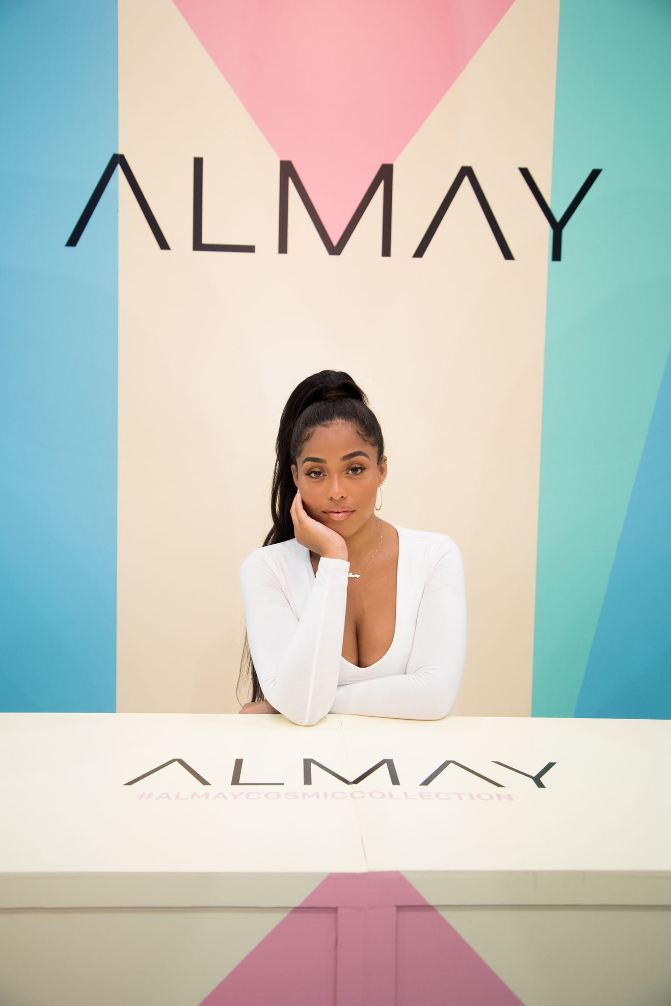 Model and influencer Jordyn Woods posing at the counter in front of the geometric Almay Cosmic Collection backdrop at a beauty brand activation in Los Angeles