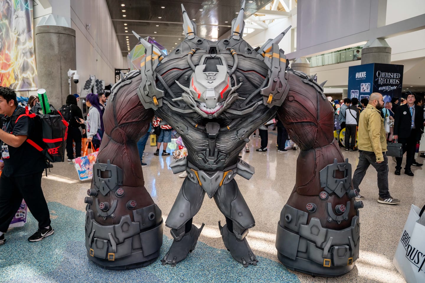 A cosplayer in a towering armored mech suit walking the Anime Expo convention floor