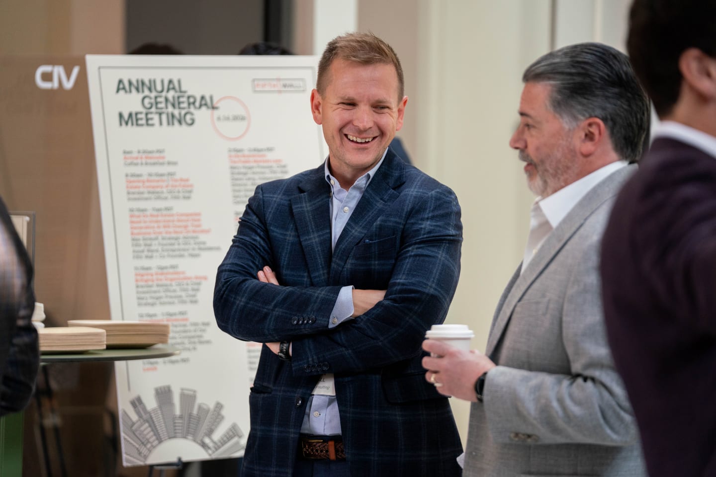 Executives talking beside an annual general meeting agenda board at a corporate event
