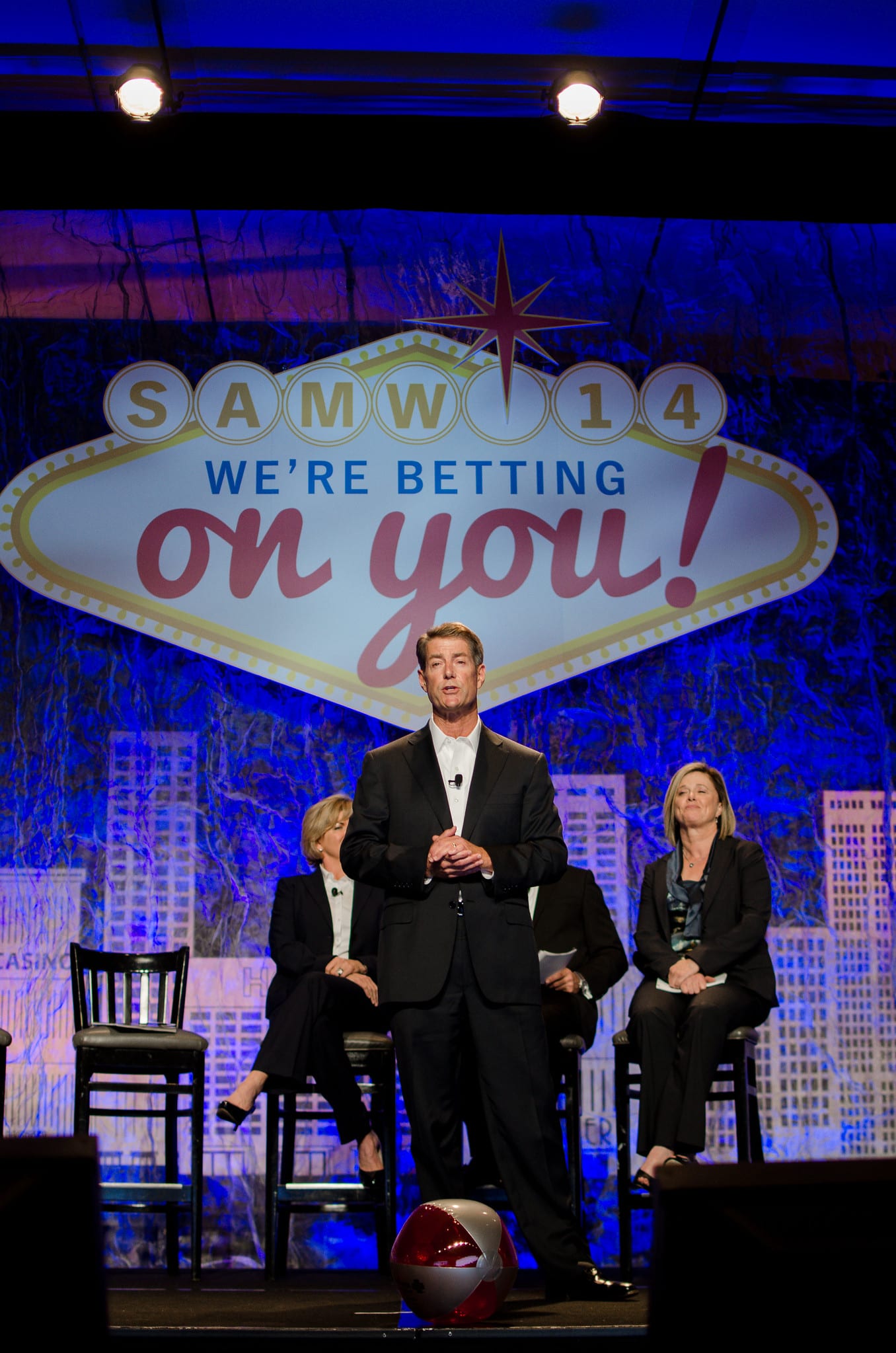 A speaker on a lit stage in front of a Las Vegas-themed “We’re Betting on You” screen at an Anthem Blue Cross meeting