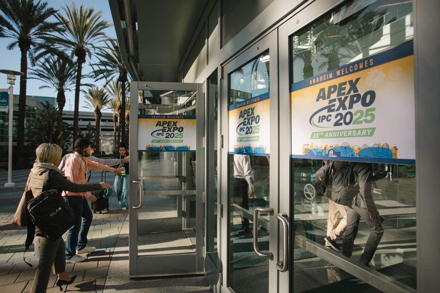 Attendees entering through glass doors branded “Anaheim welcomes APEX EXPO IPC 2025” at the Anaheim Convention Center