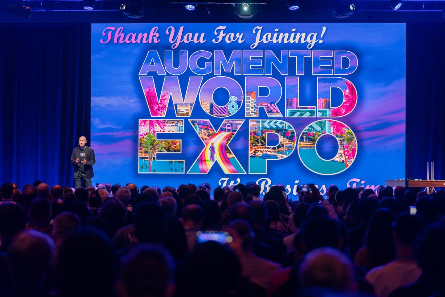 A speaker on stage in front of a packed audience under the Augmented World Expo screen at the Long Beach Convention Center