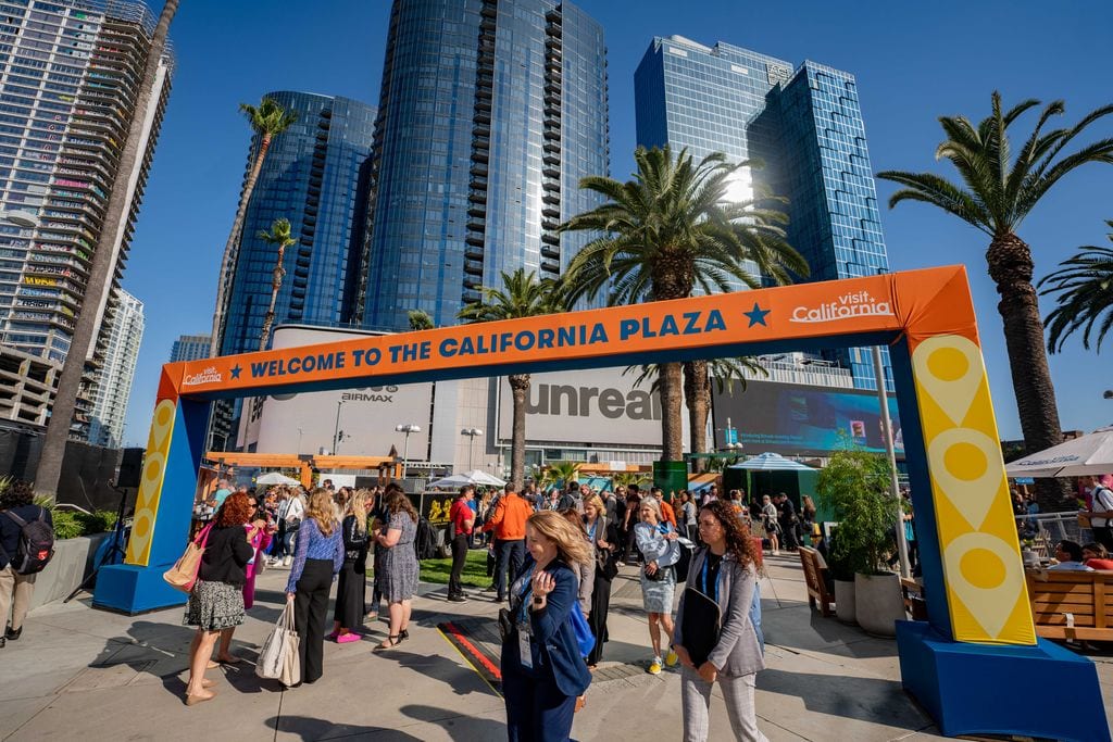 Attendees walking under a Welcome to the California Plaza arch outside the IPW travel trade show