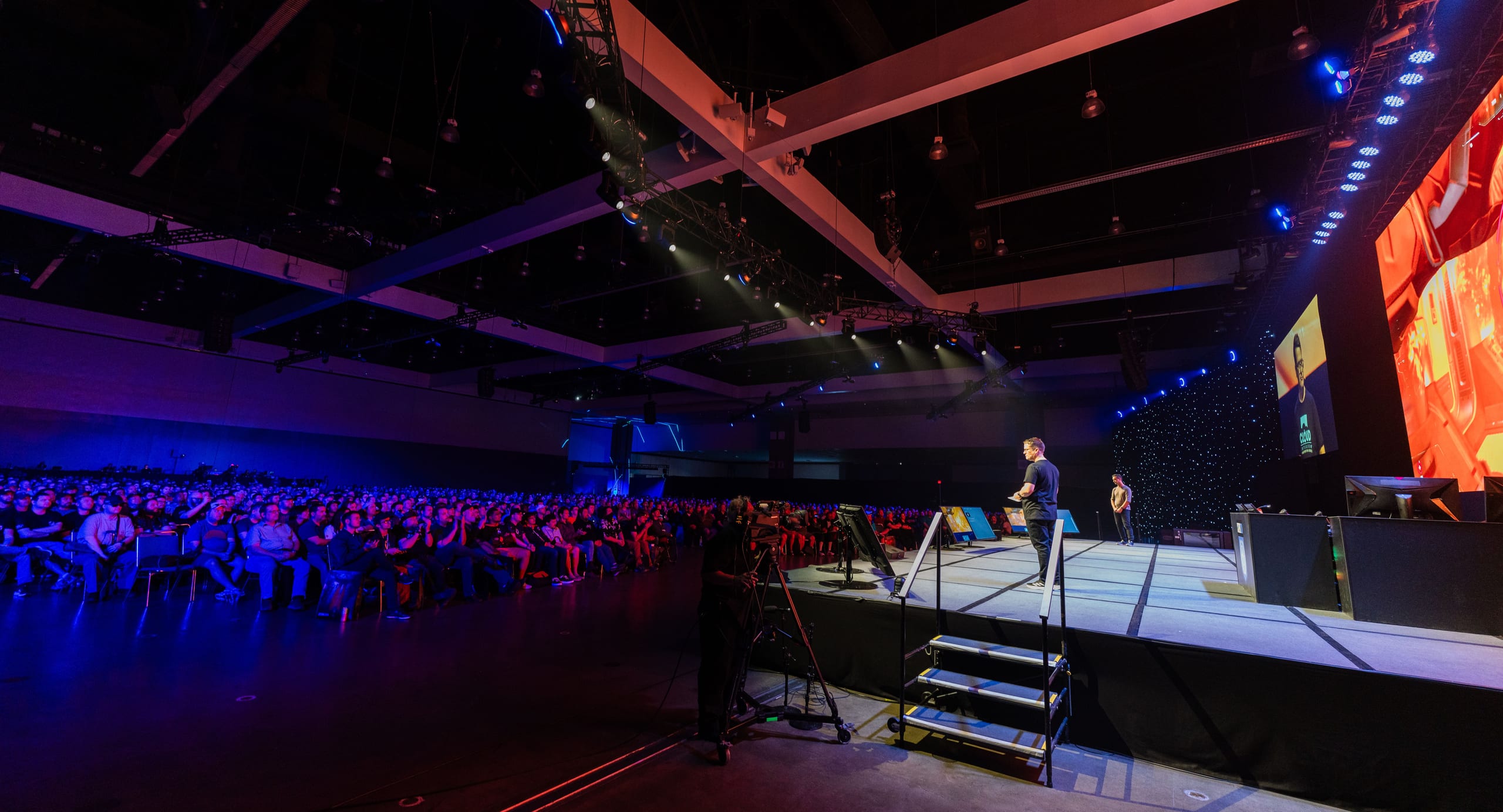 A wide view of the CitizenCon main stage with a speaker addressing a blue-lit crowd of thousands in a darkened hall at the Los Angeles Convention Center
