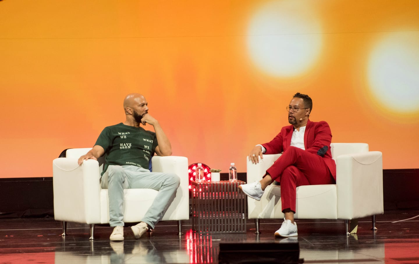 The rapper Common in a red suit speaking in a fireside chat on an orange-lit corporate stage in Las Vegas