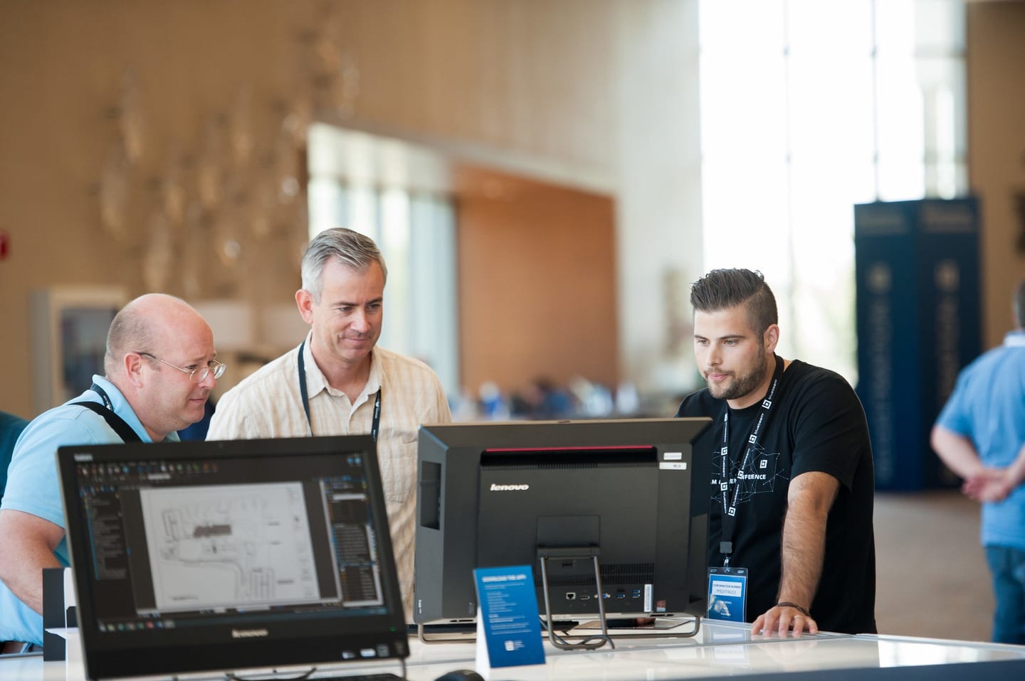 Attendees with badges reviewing software on screens at a tech conference demo station