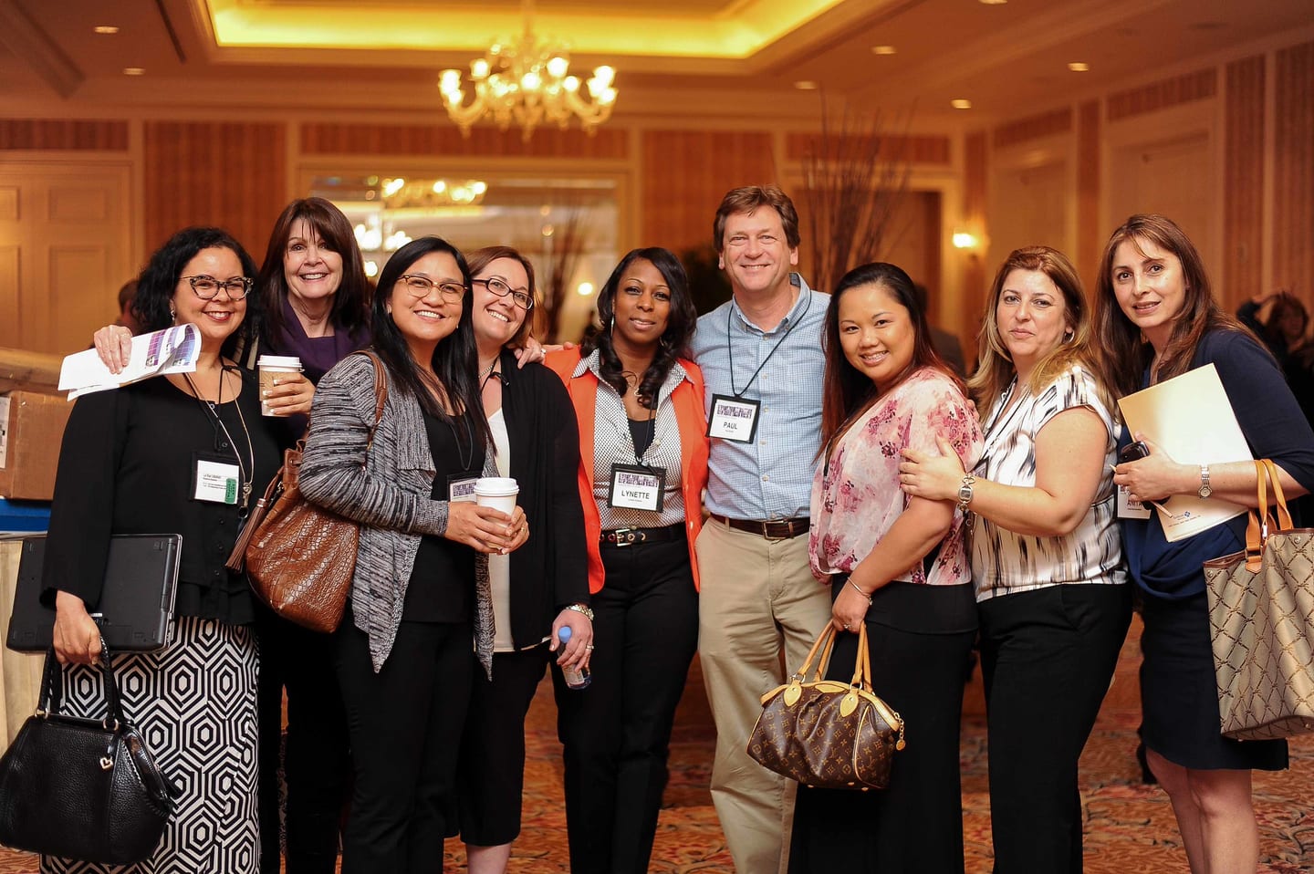 Eight colleagues in business attire posing together with conference lanyards at a San Diego hotel