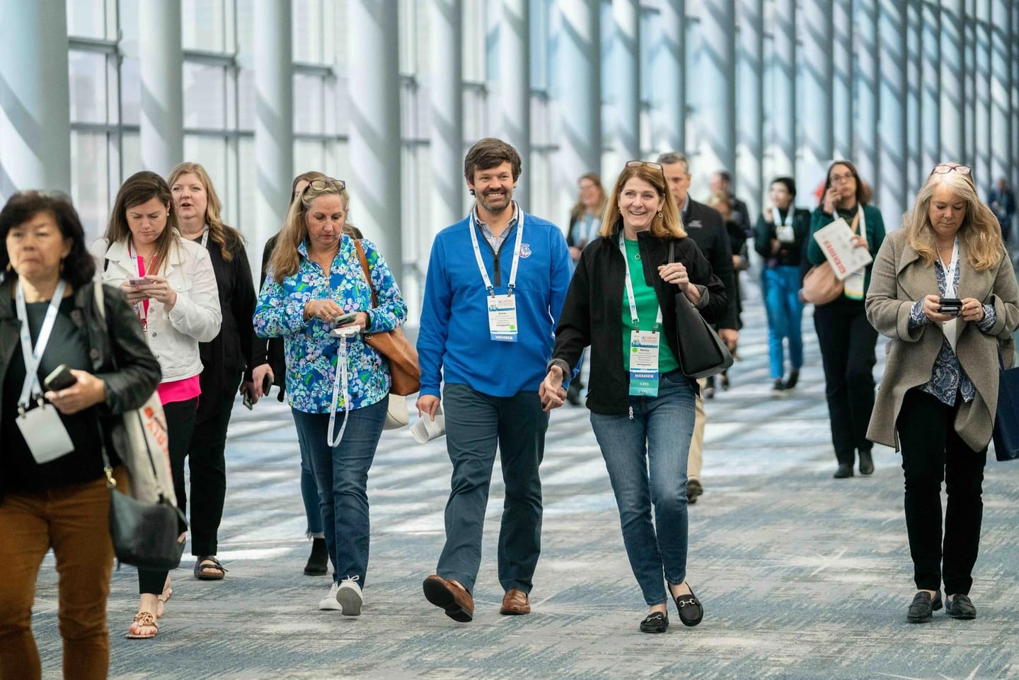 Conference attendees with lanyards walking through a bright glass convention center concourse