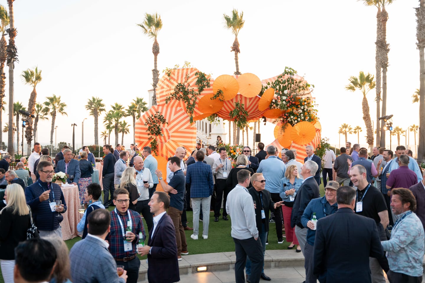 Business guests networking at an outdoor corporate reception at dusk with palm trees and a lit installation
