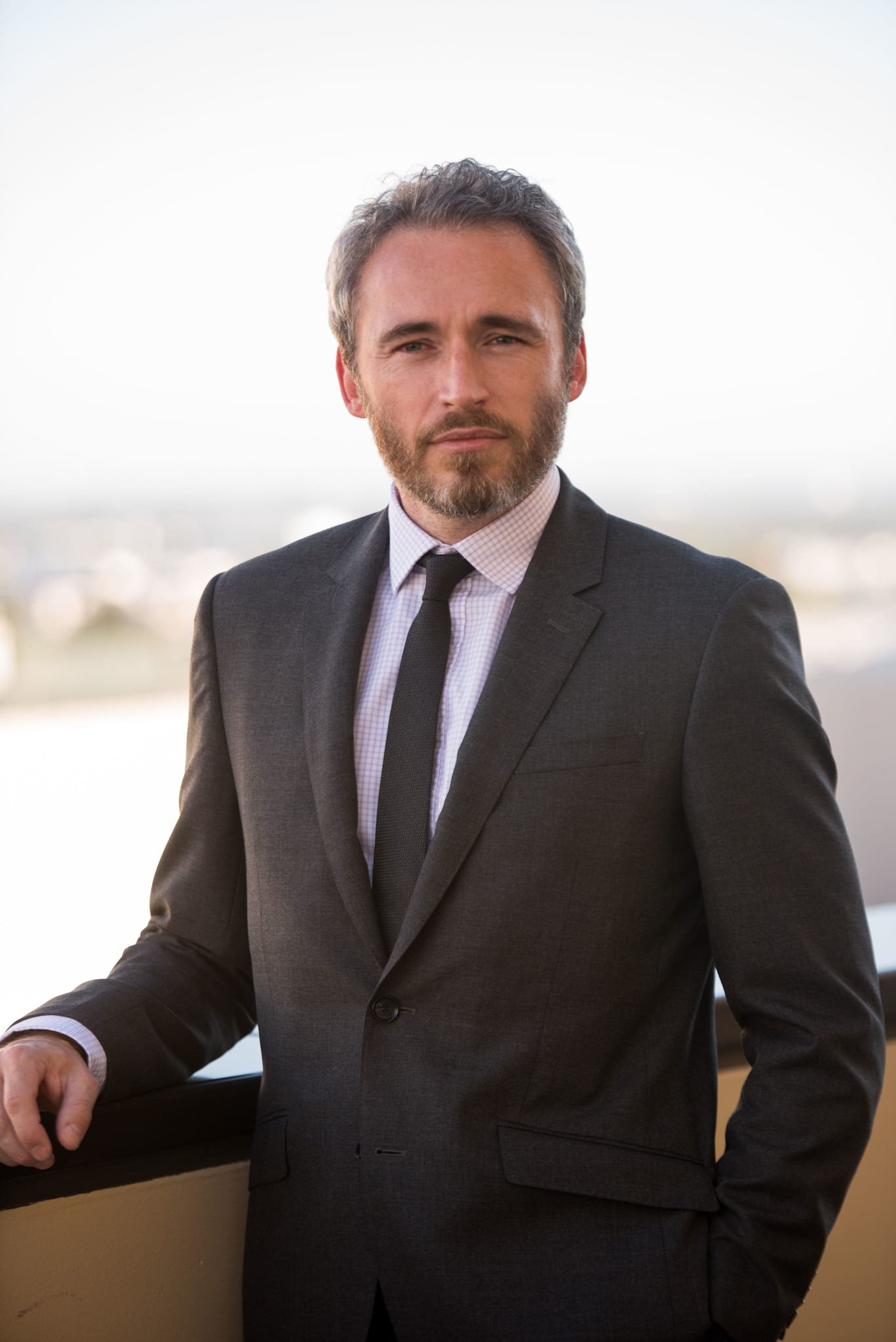 An executive in a gray suit photographed on a rooftop terrace at golden hour in Los Angeles