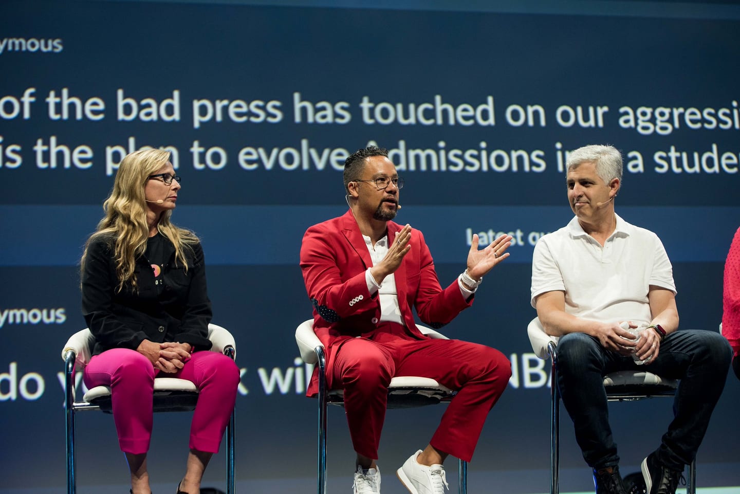 Three panelists seated on a pink-and-red lit corporate main stage in Las Vegas