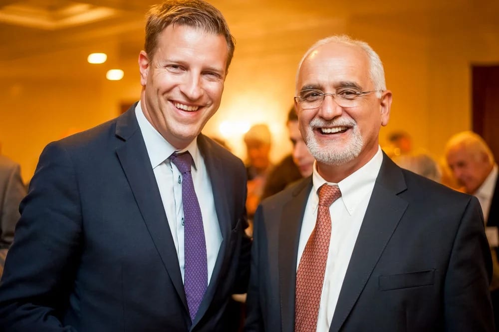 Two businessmen in suits smiling together in warm light at a corporate retreat in Santa Monica