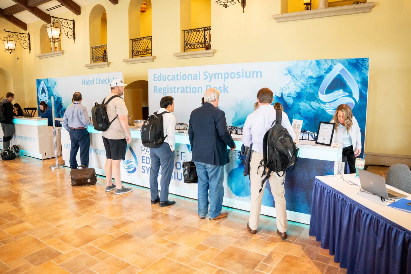 Attendees checking in at an educational symposium registration desk at a hotel conference