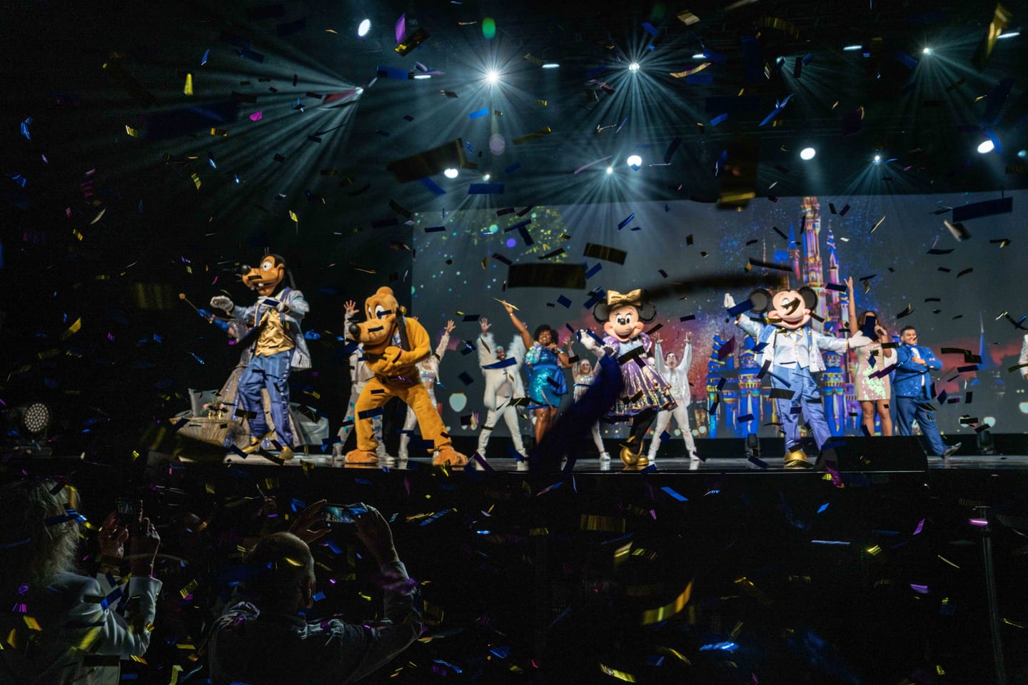 Mickey, Minnie, Pluto and dancers on stage under confetti and a castle backdrop during the Disney Destinations entertainment showcase at IPW