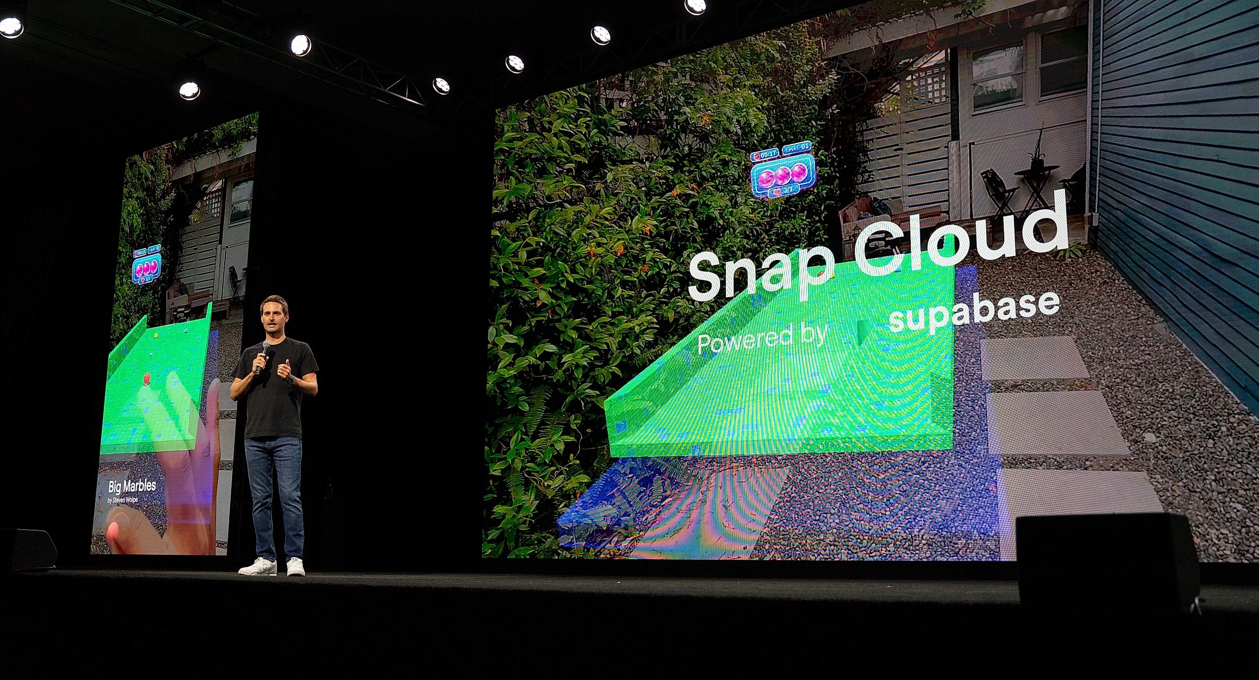 Snap CEO Evan Spiegel on stage with a microphone presenting Snap Cloud on the screens behind him at the Augmented World Expo in Long Beach