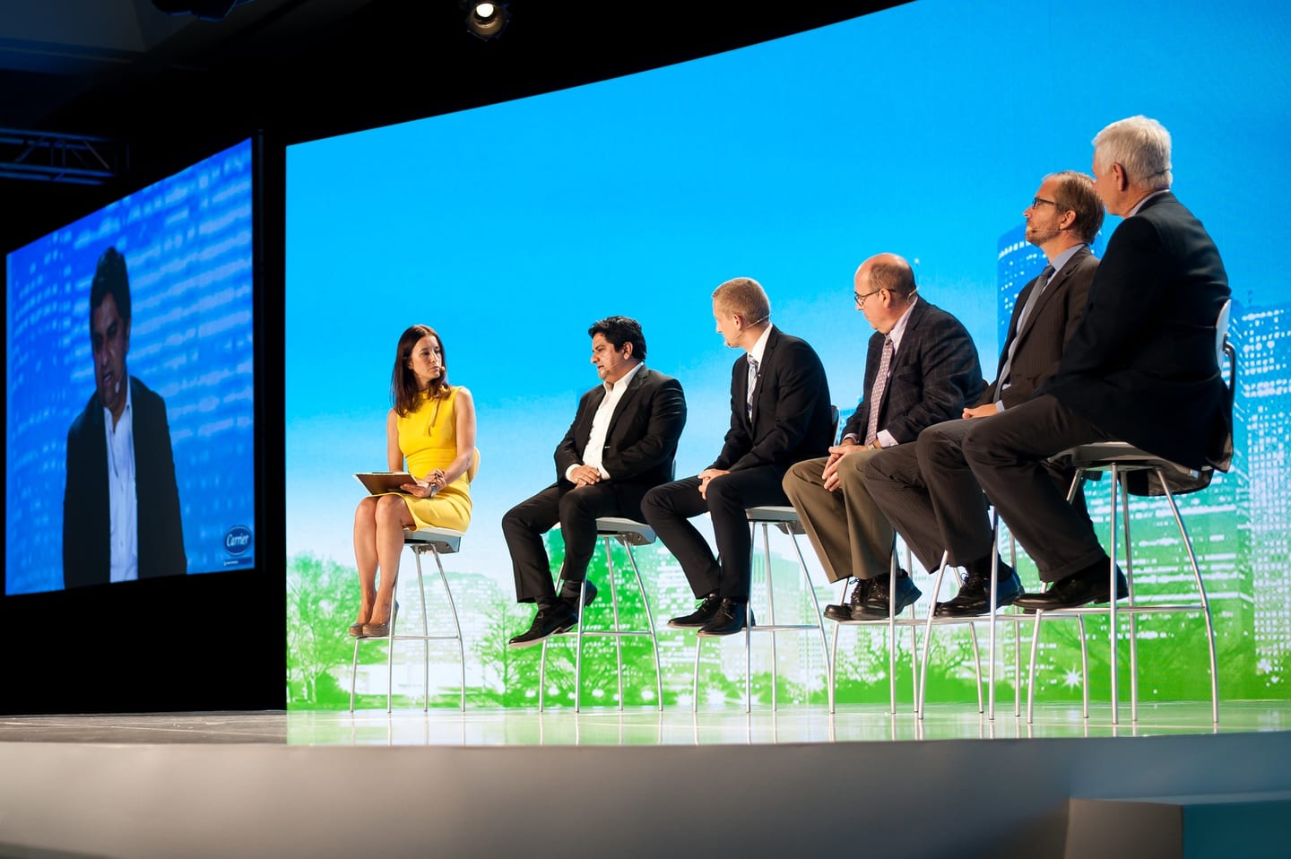 Five panelists seated on stools on a bright main stage with a sky-blue LED backdrop at the Greenbuild conference in downtown Los Angeles