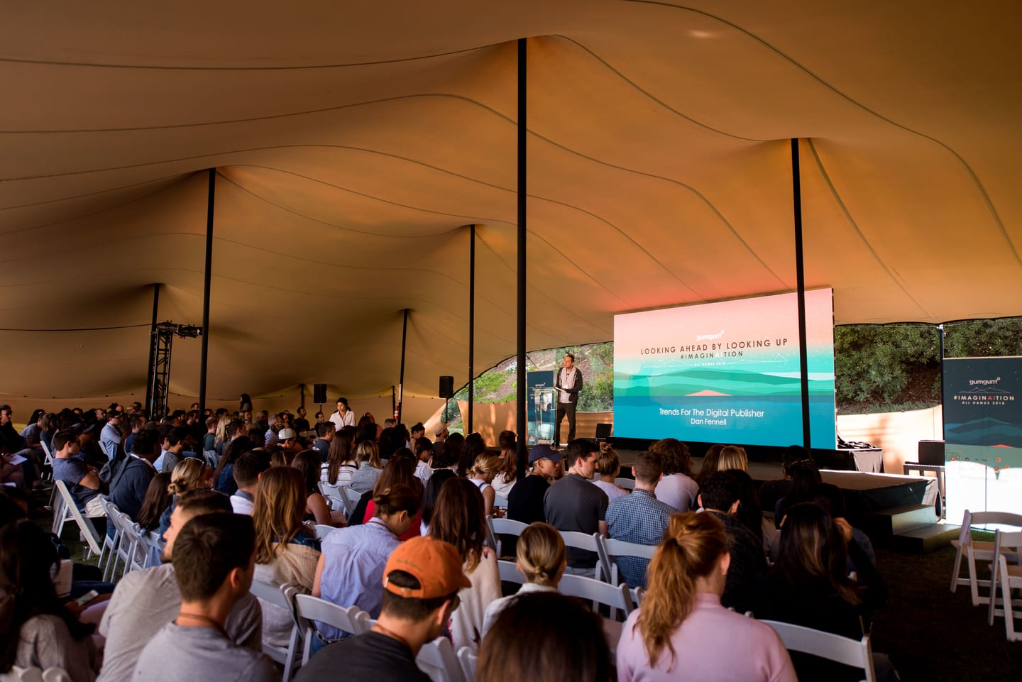 A speaker presenting beneath a large tent to a full seated audience at GumGum Imagination