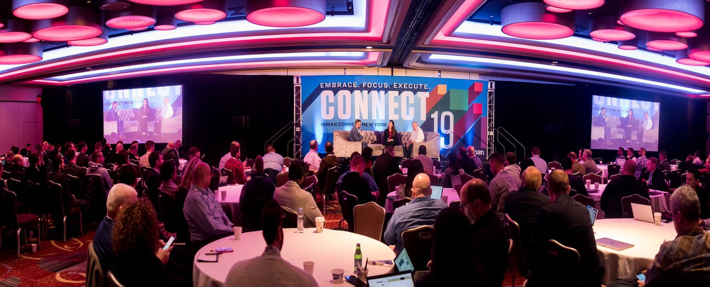 A wide view of the Inman Connect New York ballroom with a glowing pink ceiling ring over attendees seated at rounds