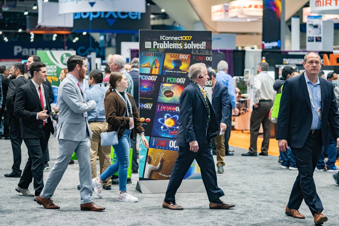 Attendees moving through a busy IPC APEX EXPO exhibition floor beside an iConnect007 industry display