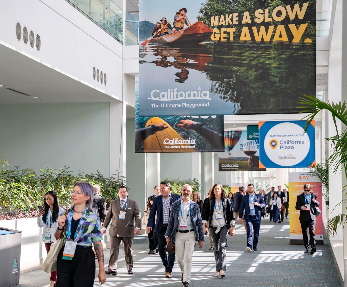 Attendees walking a convention concourse under large California travel banners at the IPW trade show