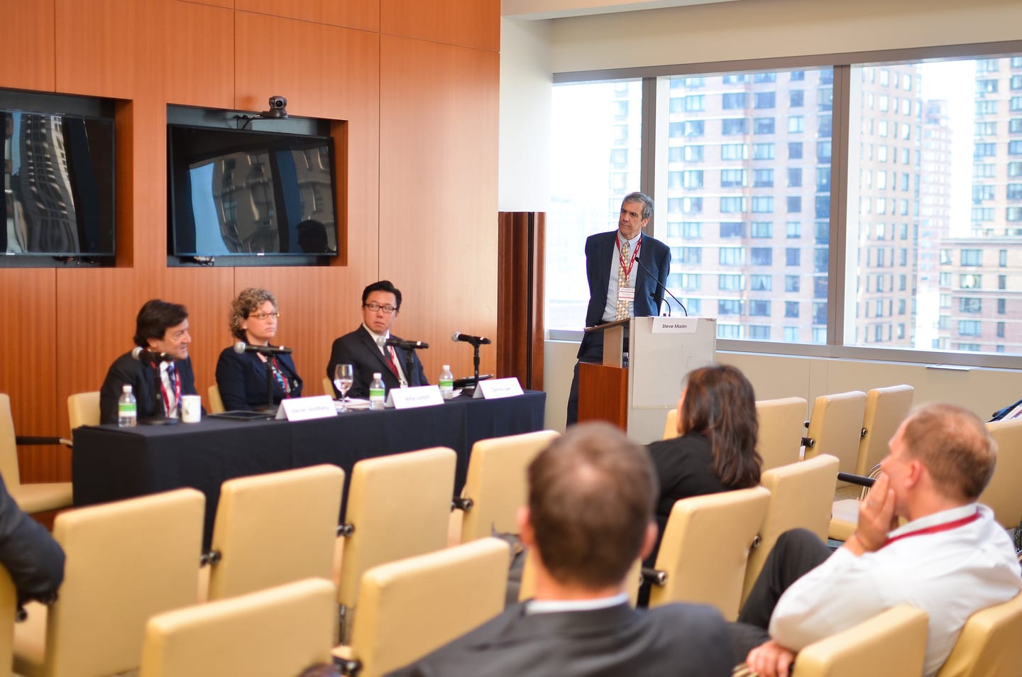 Panelists at a table beside floor-to-ceiling windows with the Manhattan skyline behind them during a Linedata session