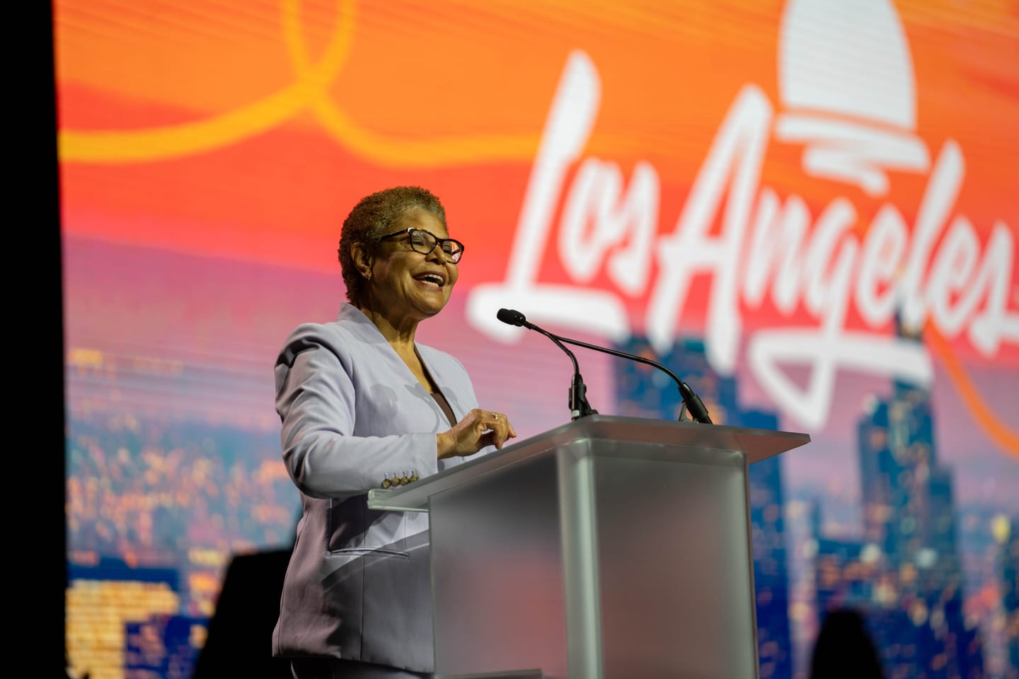 Los Angeles Mayor Karen Bass speaking at a podium in front of a Los Angeles skyline screen at IPW