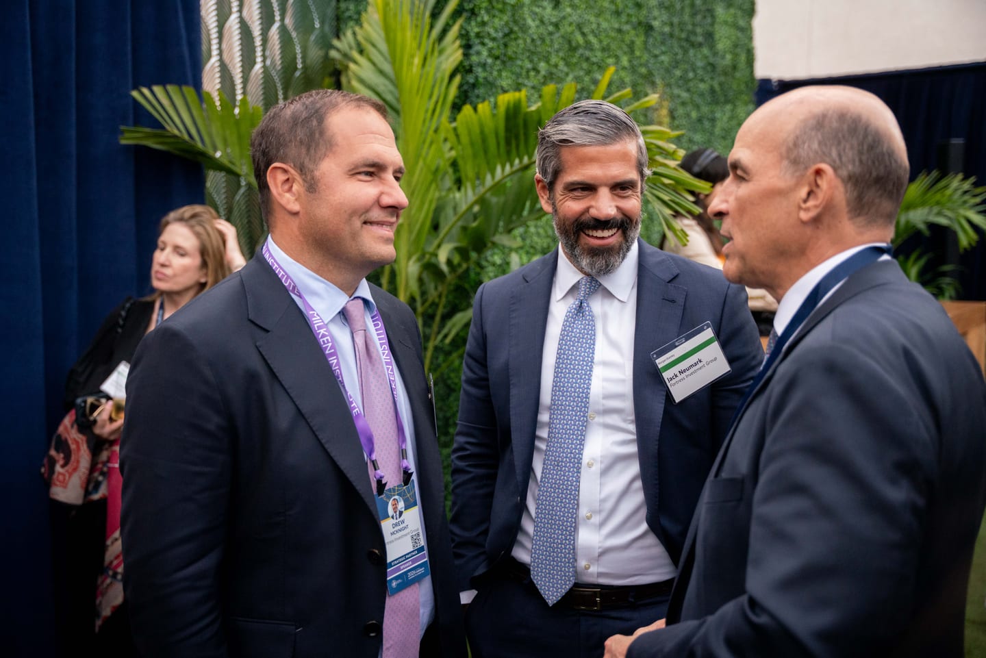 Three executives in suits talking and laughing at a reception during the Milken Institute Global Conference in Los Angeles
