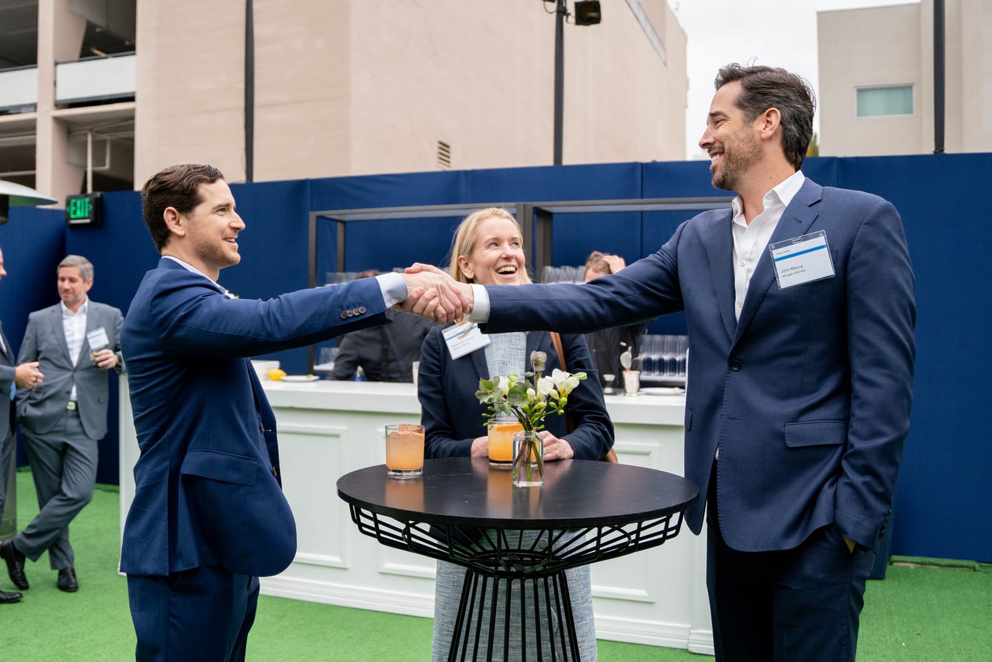 Two executives shaking hands over cocktails at a Morgan Stanley and Sotheby’s networking reception in Los Angeles