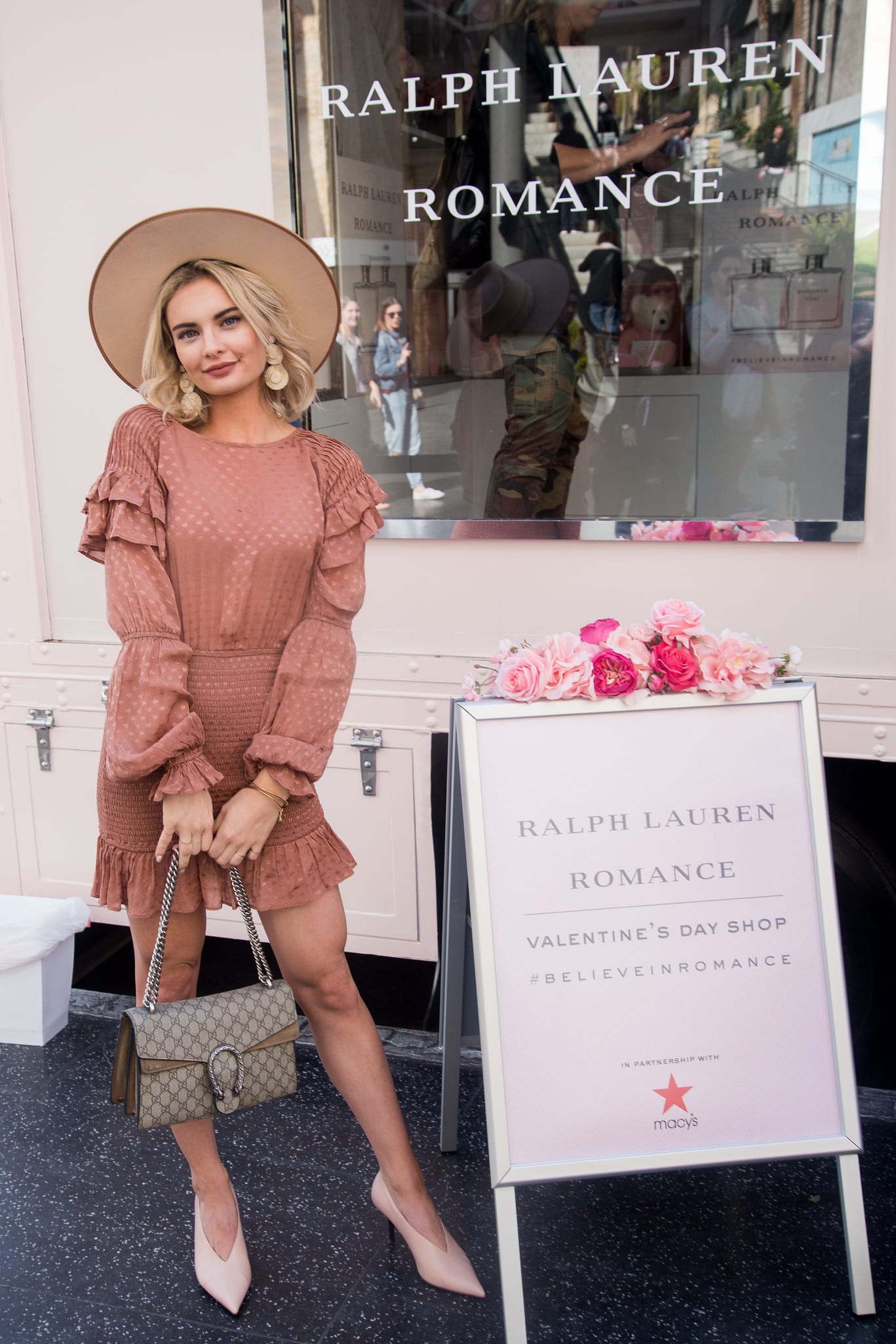 Influencer in a hat posing beside the Ralph Lauren Romance Valentine’s shop signage and fragrance window at Ovation Hollywood