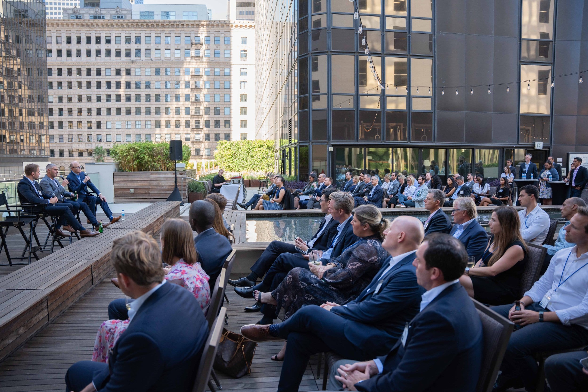 Executive fireside chat before a seated audience on a Downtown Los Angeles rooftop at dusk, skyline behind