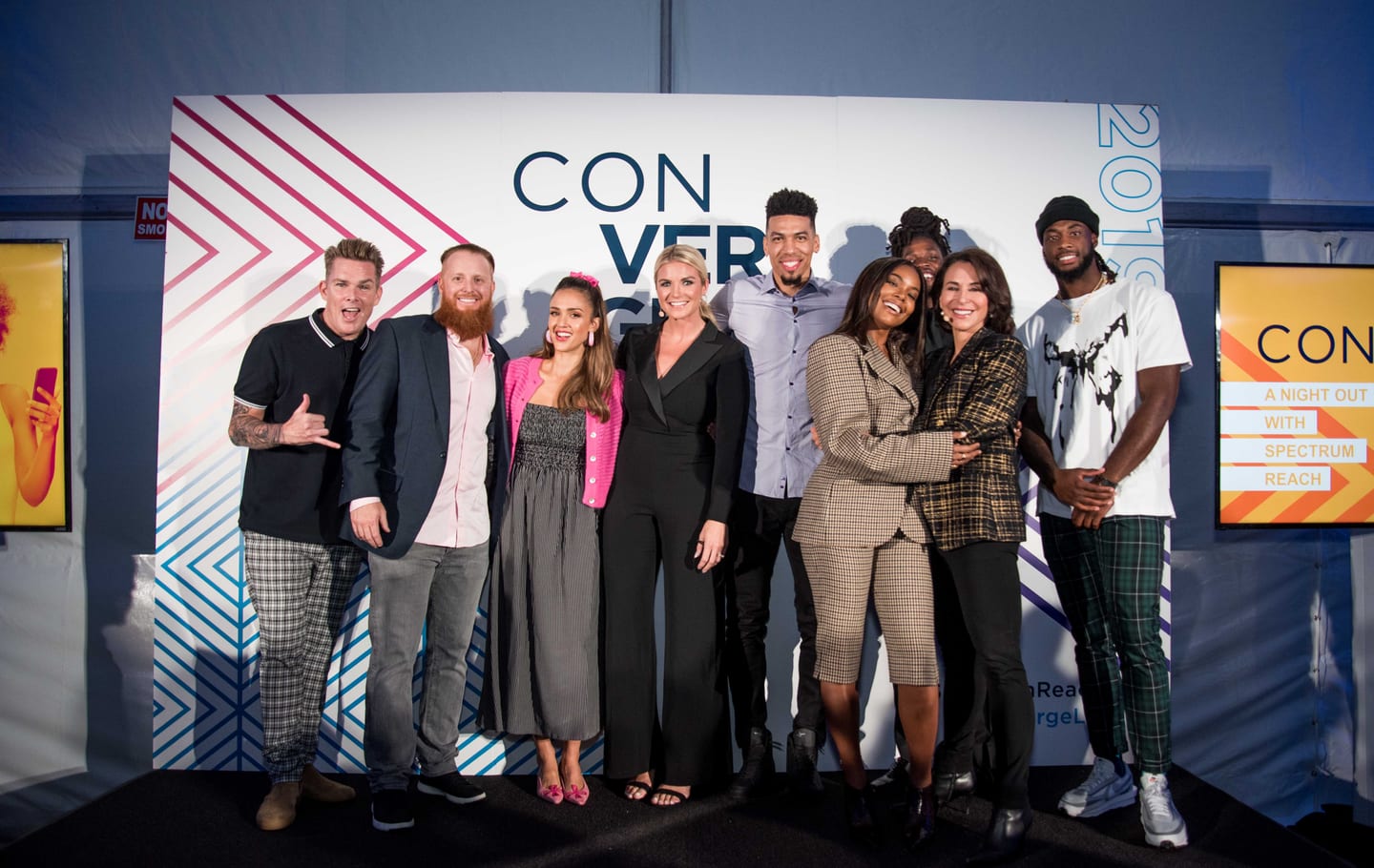 Nine guests posed together laughing on a step-and-repeat reading CONVERGE 2019, with A Night Out With Spectrum Reach signage on the wall beside them