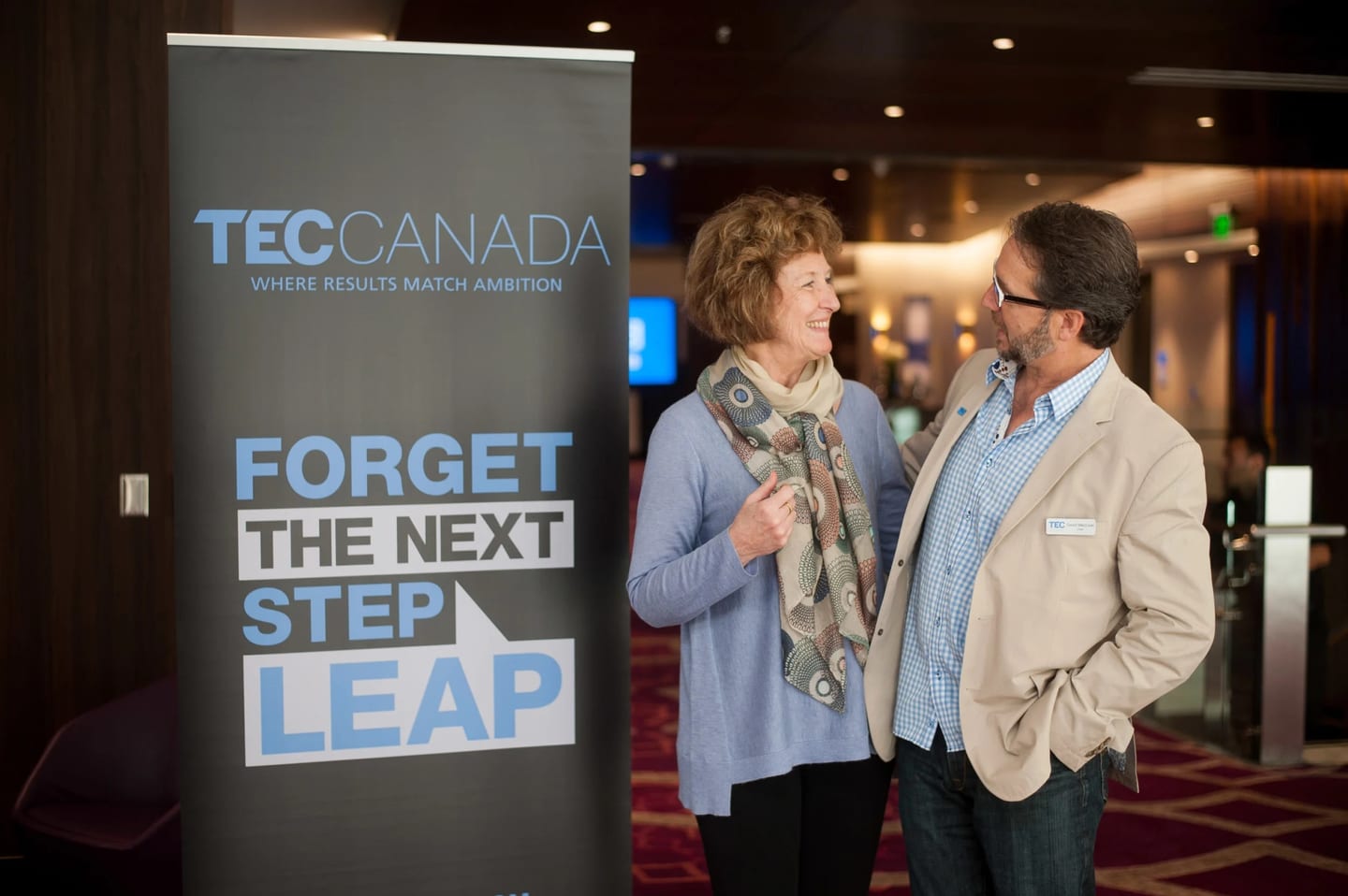 Two guests in conversation beside a TEC Canada banner at a corporate event