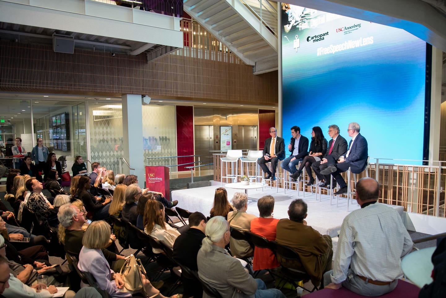 Two people in a fireside chat on a low stage in front of a seated audience at USC