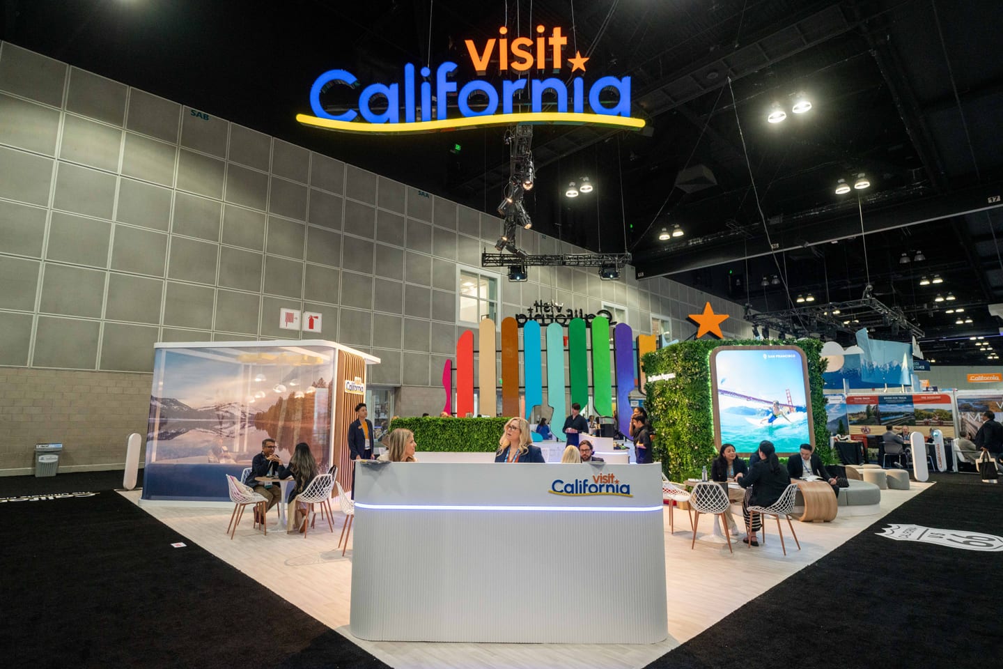 The Visit California exhibitor booth with a lit neon sign on the IPW trade show floor