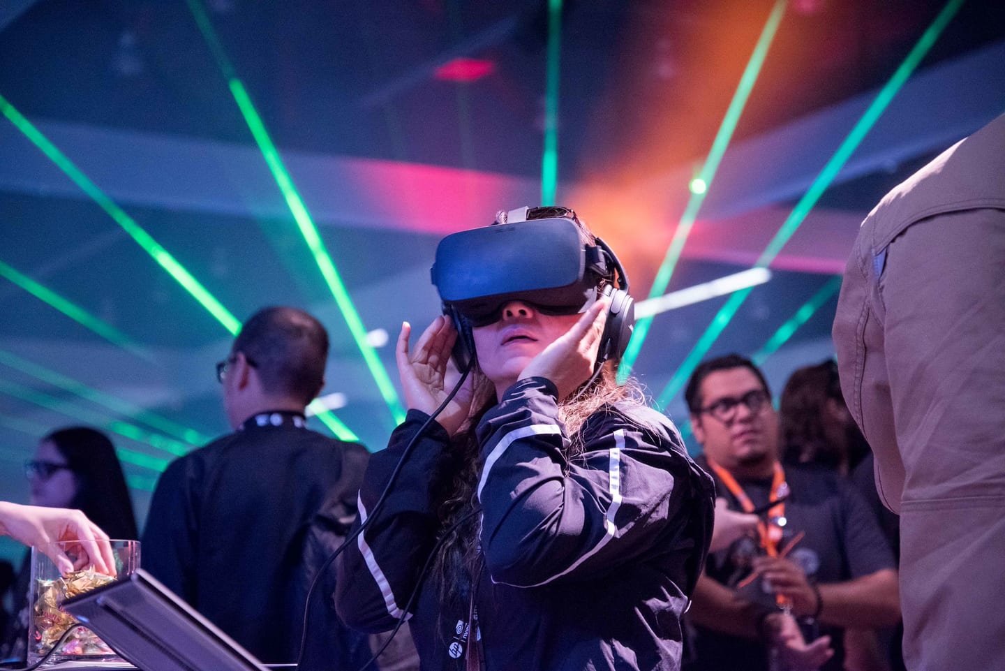 An attendee wearing a VR headset amid green laser beams and colored lighting on the show floor at VRLA, the Virtual Reality Los Angeles expo