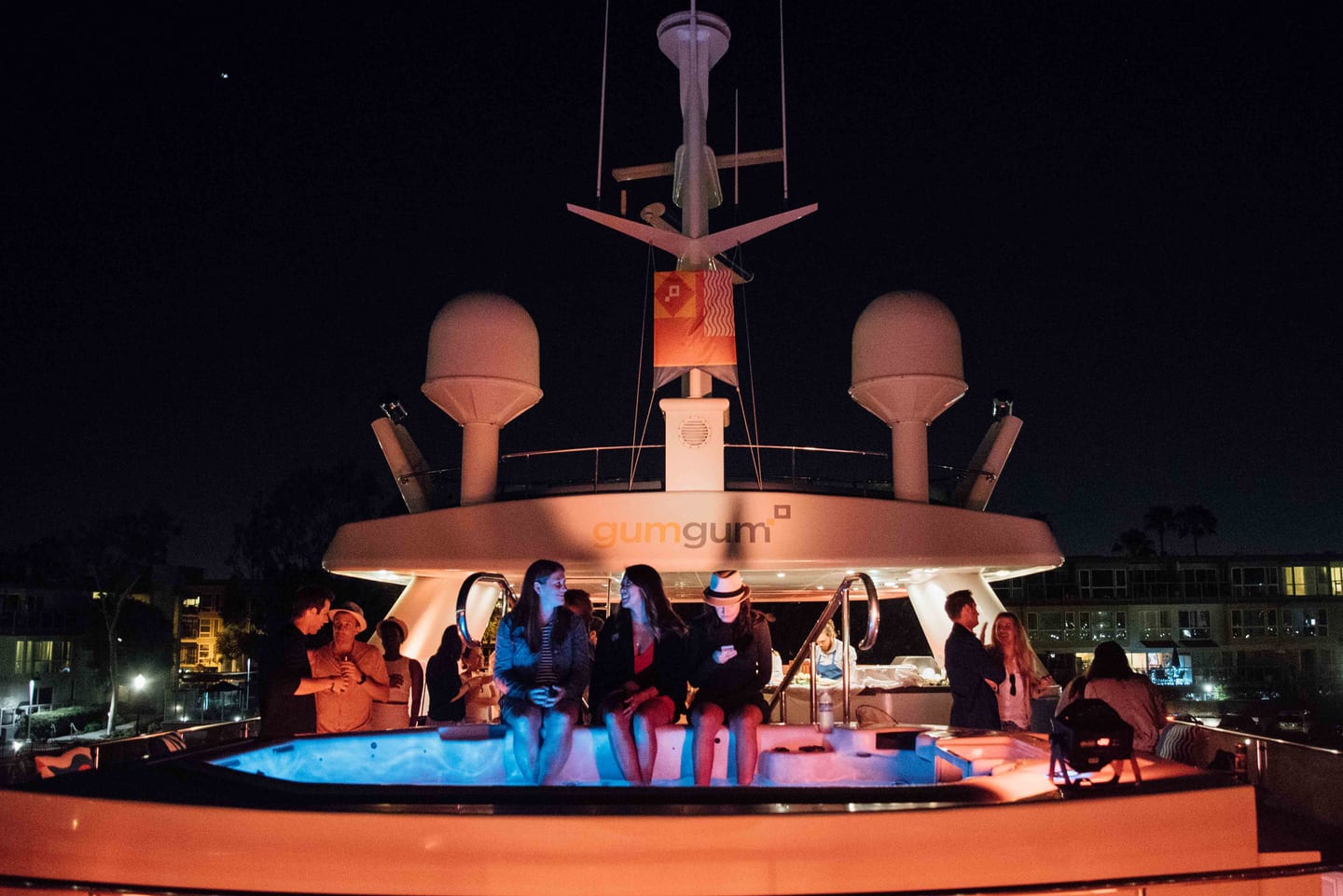 A lit yacht deck at dusk with guests seated around a lounge on the water